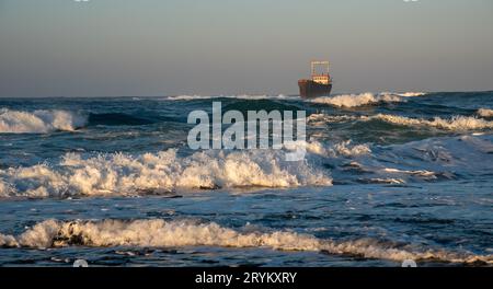 Verlassenes Schiff im stürmischen Meer mit großen Windwellen bei Sonnenuntergang. Schiffbruch im Ozean Stockfoto