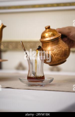 Die Hand eines Mannes gießt Tee aus einer Teekanne aus Kupfer in eine türkische Tasse. Stockfoto