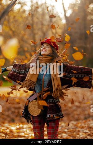 Hallo Herbst. Glückliche moderne Frau in rotem Hut mit Schal und Tasche, die im Stadtpark Freude macht. Stockfoto