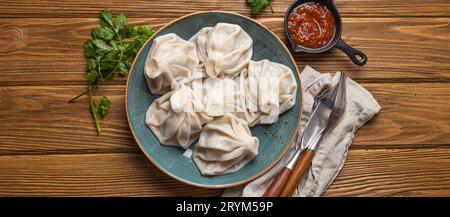 Georgianische Khinkali-Knödel auf Teller mit roter Tomatensauce und frischem Koriander von oben, rustikaler hölzerner Hintergrund, traditioneller Di Stockfoto