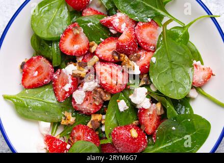 Nahaufnahme des leichten gesunden Sommersalats mit frischen Erdbeeren, Spinat, Rahmkäse und Walnüssen auf weißer Keramikplatte, weiß Stockfoto