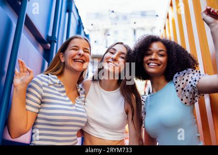 Drei süße Teenager-Mädchen in lässiger Kleidung auf bunten Versandbehältern. Stockfoto