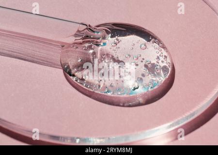 Pipettieren Sie mit einer Probe des kosmetischen Gels in einer Petrischale auf pinkfarbenem Hintergrund mit harten Schatten Stockfoto