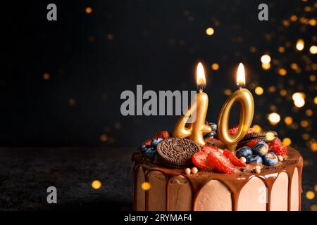 Schokoladen-Geburtstagskuchen mit Beeren, Keksen und Zahl vierzig goldenen Kerzen auf schwarzem Hintergrund, Kopierraum Stockfoto