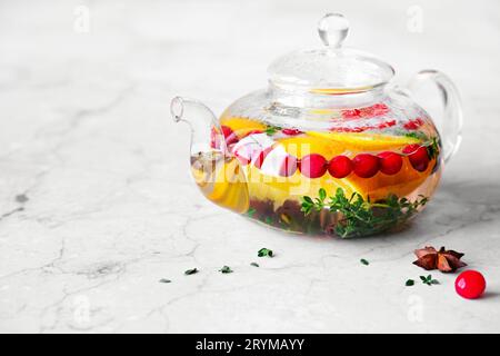 Immunitätssteigerungsgetränk. Thymian-Tee mit Preiselbeeren, Orange und Gewürzen in Glas-Teekanne auf Marmortisch Stockfoto