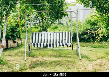 Schwingen Sie zwischen Bäumen im Garten. Cottagecore und Staycation zu Hause. Sommergarten mit Platz für Erholung und Entspannung Stockfoto