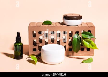 Mockup-Gläser für Branding und Label. Kosmetikprodukte auf Ständer aus Ziegeln und grünen Blättern. Minimal Creative Beauty Con Stockfoto