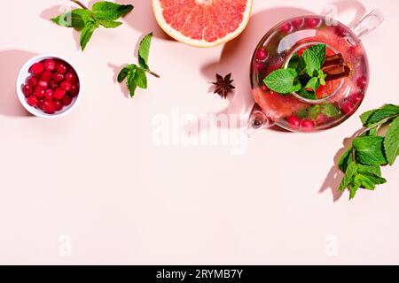 Immunitätssteigerungsgetränk. Minztee mit Preiselbeeren, Grapefruit und Gewürzen in Glas-Teekanne auf rosa Tisch, trendige Schatten Stockfoto