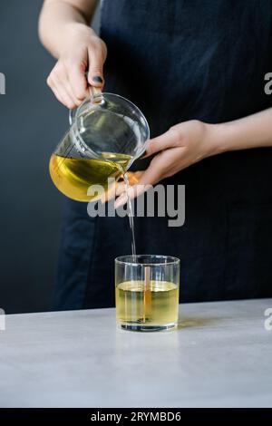 Das Mädchen gießt Wachs in Glasgläser mit Dochten. Stockfoto