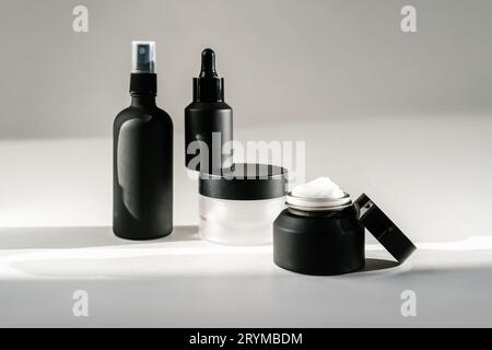 Schwarze Kosmetikflaschen auf einem Hintergrund, der von Sonnenlicht durchflutet ist. Stockfoto
