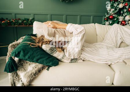 Eine gestresste Frau versteckte ihr Gesicht in einem Kissen, während sie auf dem Sofa im Wohnzimmer lag. Burnout und Depression während der Christma Stockfoto