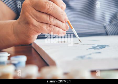 Attraktive alte Frau malte nach Zahlen in der Nähe zu Hause. Inspirierende Hobby- und Kunsttherapie. Selektiver Fokus Stockfoto