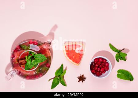 Immunitätssteigerungsgetränk. Minztee mit Preiselbeeren, Grapefruit und Gewürzen in Glas-Teekanne auf rosa Tisch, trendige Schatten Stockfoto