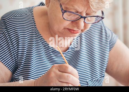 Attraktive alte Frau, die zu Hause nach Zahlen malte. Inspirierende Hobby- und Kunsttherapie. Selektiver Fokus Stockfoto