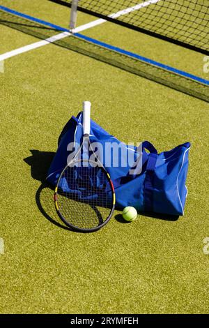 Tennisschläger, Ball und Sporttasche auf dem Boden im Netz auf einem sonnigen Rasenplatz im Freien, Kopierbereich Stockfoto