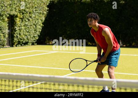 Ein birassistischer Mann mit Schläger, der darauf wartet, dass der Ball auf einem sonnigen Tennisplatz im Freien zurückkehrt, Kopierraum Stockfoto