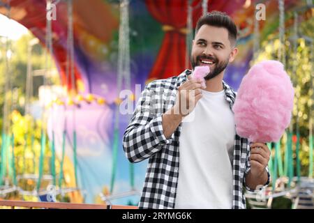 Glücklicher junger Mann, der auf der Messe Zuckerwatte isst, Platz für Text Stockfoto
