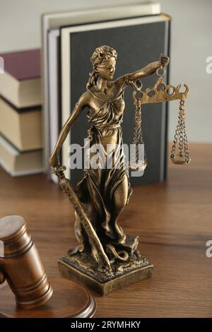 Figur der Lady Justice, Hammer und Bücher auf Holztisch im Innenbereich. Symbol der gerechten Behandlung nach dem Gesetz Stockfoto