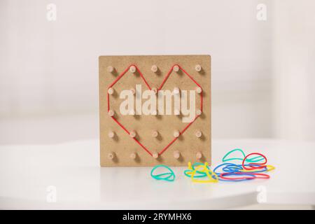 Geoboard aus Holz mit Gummibändern auf weißem Tisch im Innenbereich. Lernspielzeug zur Förderung der motorischen Fähigkeiten Stockfoto