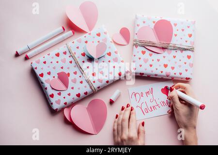 Draufsicht der weiblichen Hände auf rosa Hintergrund mit Geschenken schreiben valentine Karte BE MY VALENTINE Stockfoto