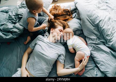 Mama mit zwei kleinen Kindern liegt morgens auf dem Bett und genießt Beziehungen und Mutterschaft. Stockfoto