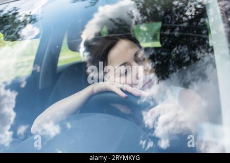 Junge Fahrerin am Lenkrad ihres Autos, sehr müde, beim Fahren einschlafend Stockfoto