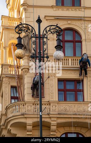 Prag, CZ - 28. oktober 2021:zwei Arbeiter mit Staubsaugern, die hoch oben auf der Rupe hängen und Staub an der Fassade eines Hotels in Prag reinigen. Sauber Stockfoto