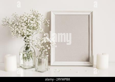 Kerzen, gypsophila-Blumen und Bilderrahmen auf Tischwandhintergrund. Modell Vorderansicht Stockfoto