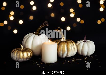 Festliche Komposition zu Halloween oder Thanksgiving mit goldenen Kürbissen und brennender Kerze auf schwarzem Hintergrund. Vorderansicht Stockfoto
