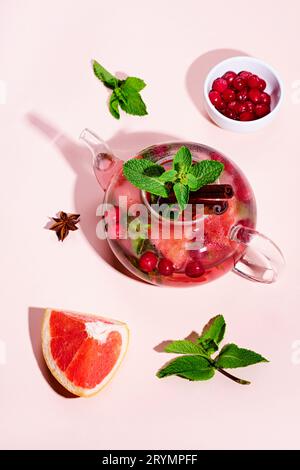 Immunitätssteigerungsgetränk. Minztee mit Preiselbeeren, Grapefruit und Gewürzen in Glas-Teekanne auf rosa Tisch, trendige Schatten Stockfoto