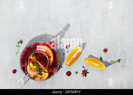 Immunitätssteigerungsgetränk. Wintertee mit Preiselbeeren, Orange, Hibiskus und Gewürzen in Glaskanne auf weißem Tisch Stockfoto