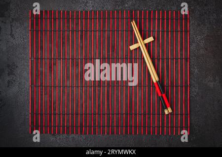 Japanische Tischeinstellung. Bambus-Essstäbchen und Matte in rot-schwarzen Farben Stockfoto