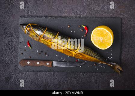 Geräucherter Makrelen Fisch, Messer und Zitrone auf schwarzem Steinschneidebrett Stockfoto