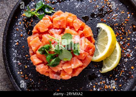 Roher Lachs, Avocado purple Zwiebel Salat serviert kulinarische Ring auf schwarze Platte. Schwarz konkreten Hintergrund Stockfoto