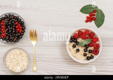 Haferbrei in Porzellanschale mit Johannisbeeren und Himbeeren, dekoriert mit Minzblättern. Stockfoto