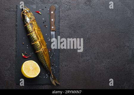 Geräucherte Makrele, Messer und Zitrone auf schwarzem Steinschneidebrett, Kopierraum Stockfoto