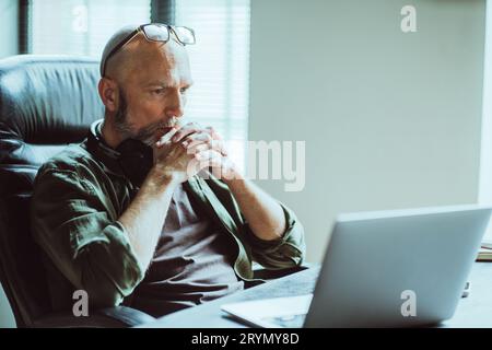 Ein Mann mittleren Alters, der sich voll auf die Arbeit konzentriert, schaut aufmerksam auf den Computer auf dem Tisch. Tief in Gedanken denkt er über Aufgabe oder Problem bei nach Stockfoto