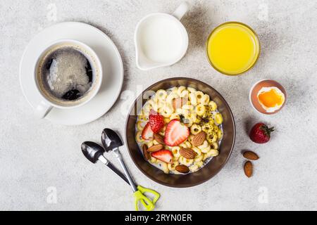 Schüssel mit Müsliringen, Erdbeeren und Milch. Frischer Kaffee, Orangensaft und Ei. Ausgewogenes Frühstückskonzept Stockfoto