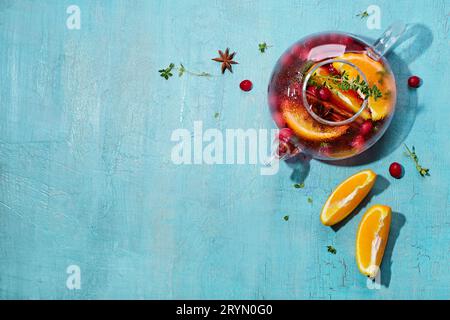 Immunitätssteigerungsgetränk. Wintertee mit Preiselbeeren, Orange, Hibiskus und Gewürzen in Glaskanne auf blauem Tisch Stockfoto