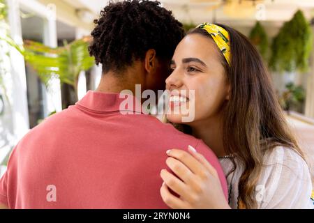 Birassistische lächelnde junge, schöne Freundin, die ihren Freund umarmt, während sie zu Hause steht Stockfoto