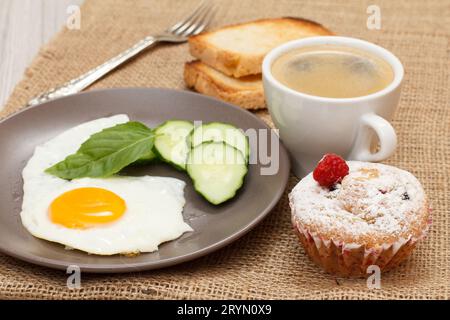 Teller mit Spiegelei, Gabel, Tasse schwarzem Kaffee, Cupcake und Toasts Stockfoto