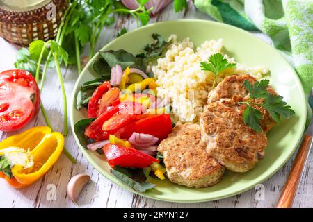 Gesunde vegane Lebensmittel, Keto- oder Paläodiäten. Hausgemachte rote Fischschnitzel mit Bulgur und frischem Gemüsesalat auf einem Holztisch. Stockfoto