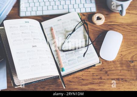 Öffnen Sie den Kalender in einem Notebook auf einem Desktop vor einem Computer. Stockfoto