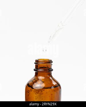 Ätherisches Öl, das aus dem bernsteinfarbenen Glasbehälter fällt. Blaue Flasche kosmetisches Öl mit einer Pipette Stockfoto