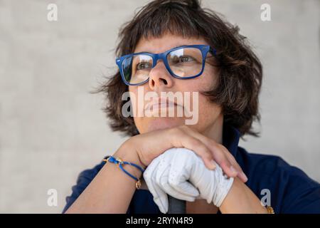 Golferin mit Brille und einem Handschuh, der sich auf ihren Golfclub legt und sich an einem sonnigen Tag in der Schweiz umsieht Stockfoto