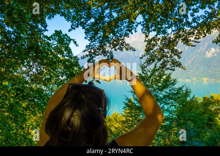 Frau, die eine Herzform vor dem Brienzersee macht mit Berg- und Baumzweig am sonnigen Sommertag in Brienz, Berner Oberland, Kanton Bern Stockfoto