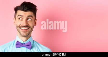 Nahaufnahme von amüsed lächelnden Kerl mit Schnurrbart, zeigen und schauen links glücklich, starren auf Logo, auf rosa Hintergrund stehen Stockfoto