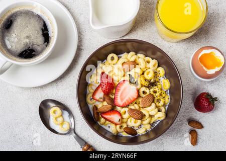 Schüssel mit Müsliringen, Cheerios, Erdbeeren und Milch. Frischer Kaffee, Orangensaft und Ei. Ausgewogenes Frühstückskonzept Stockfoto