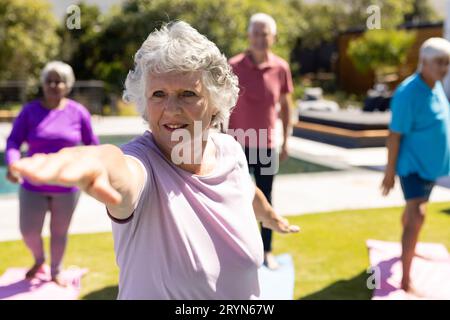 Glückliche, vielfältige ältere Freunde, die im sonnigen Garten Yoga üben Stockfoto