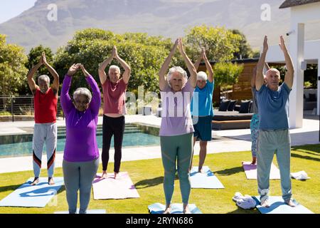 Glückliche, vielfältige ältere Freunde, die im sonnigen Garten Yoga üben Stockfoto